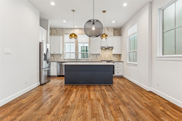 kitchen with stainless steel appliances, pendant lighting, a kitchen island, white cabinets, and backsplash