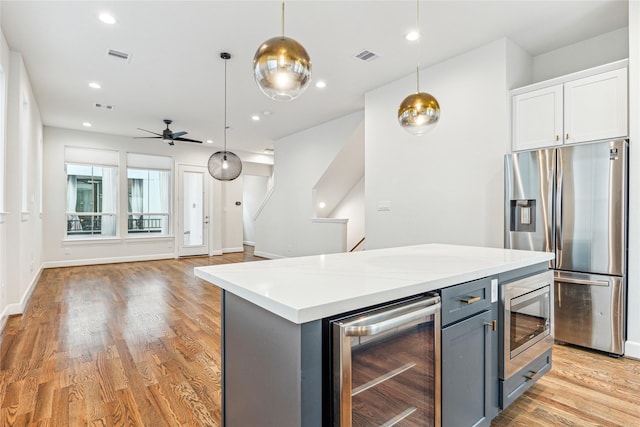 kitchen with stainless steel appliances, decorative light fixtures, white cabinetry, ceiling fan, and beverage cooler