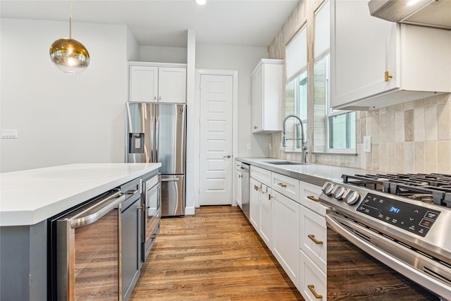 kitchen with pendant lighting, stainless steel appliances, beverage cooler, white cabinets, and sink