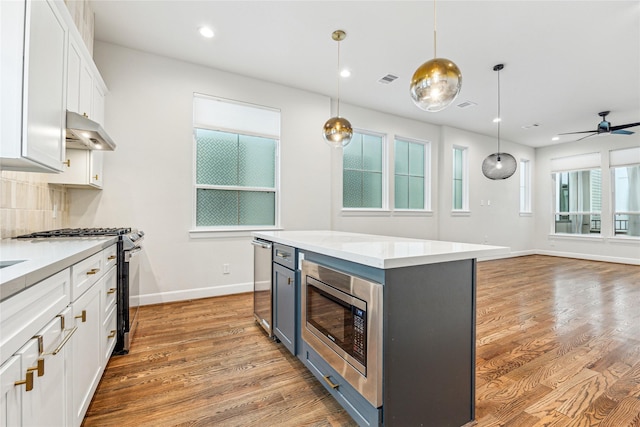 kitchen featuring appliances with stainless steel finishes, pendant lighting, a kitchen island, white cabinetry, and tasteful backsplash