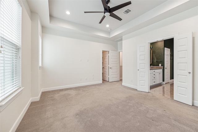 unfurnished bedroom with a raised ceiling, light colored carpet, ceiling fan, and connected bathroom