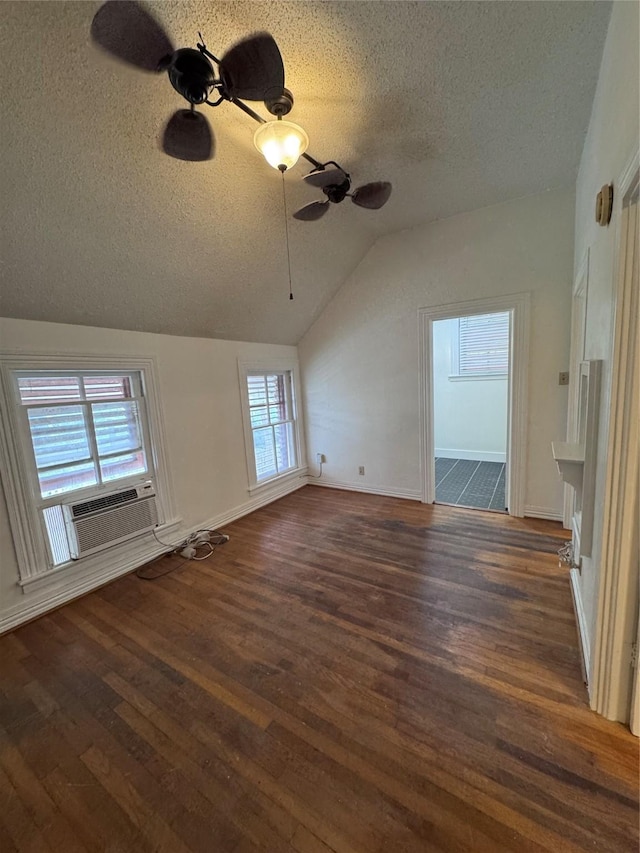 empty room with a textured ceiling, wood finished floors, cooling unit, baseboards, and lofted ceiling