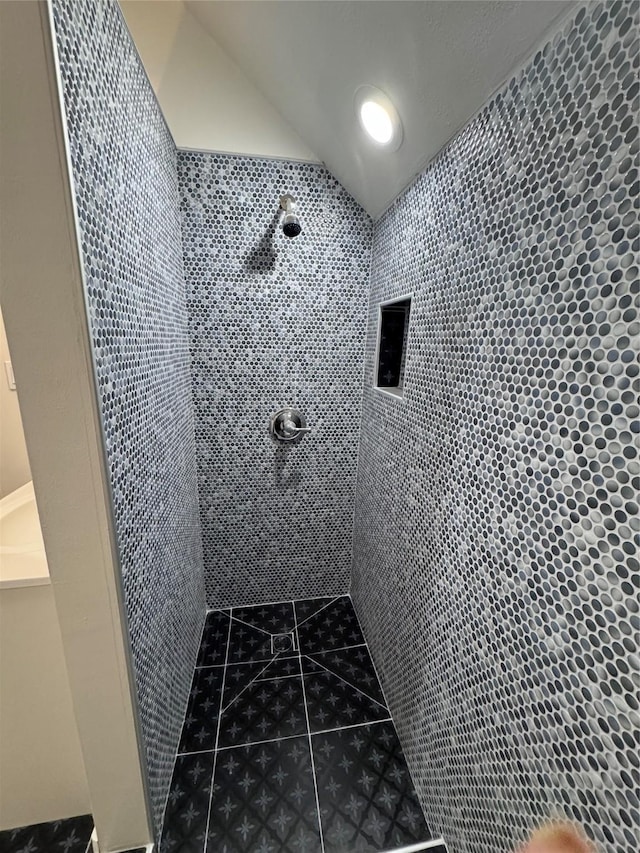 bathroom with tile patterned flooring, a tile shower, and vaulted ceiling