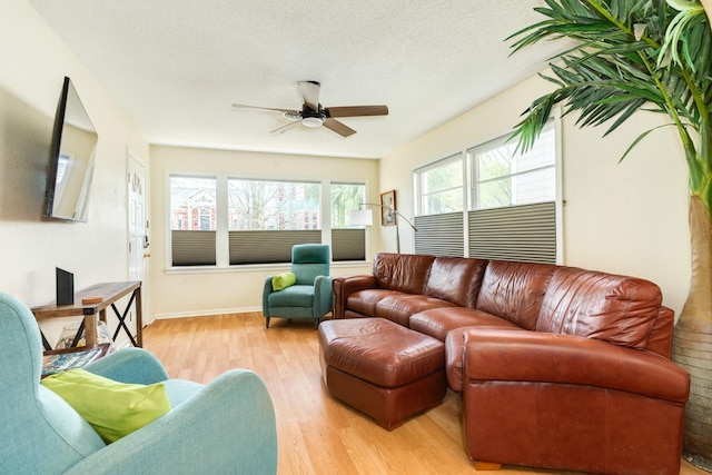 living room featuring baseboards, light wood-style floors, a ceiling fan, and a textured ceiling