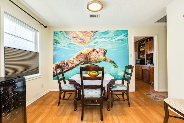 dining room with wine cooler, light wood-style flooring, visible vents, and baseboards