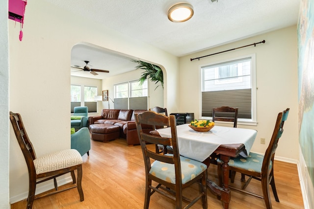 dining space featuring baseboards, arched walkways, a textured ceiling, and light wood finished floors