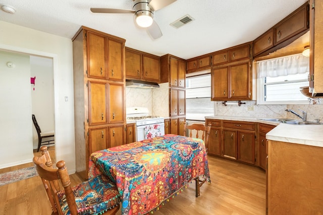 kitchen featuring visible vents, under cabinet range hood, white gas range oven, brown cabinets, and a sink