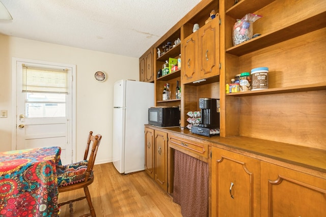 kitchen with open shelves, light wood-style flooring, freestanding refrigerator, black microwave, and brown cabinets