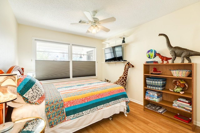 bedroom with a ceiling fan, wood finished floors, baseboards, and a textured ceiling