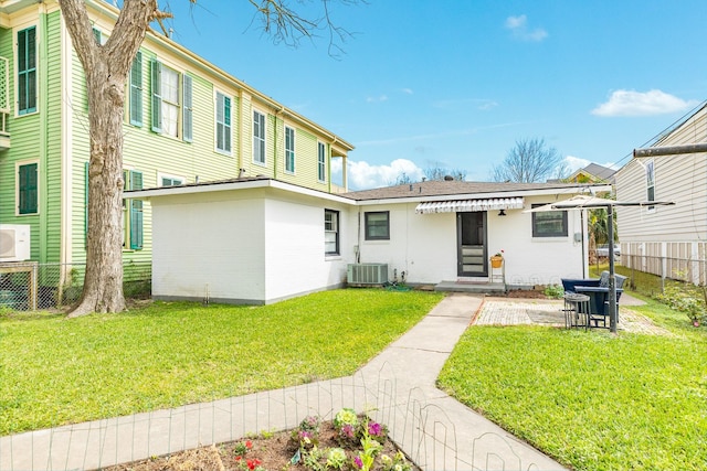 rear view of house with a yard, fence, brick siding, and cooling unit