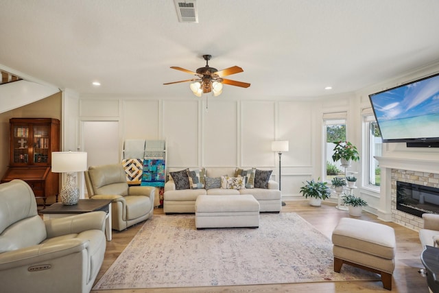 living room featuring ceiling fan, light hardwood / wood-style floors, and a stone fireplace