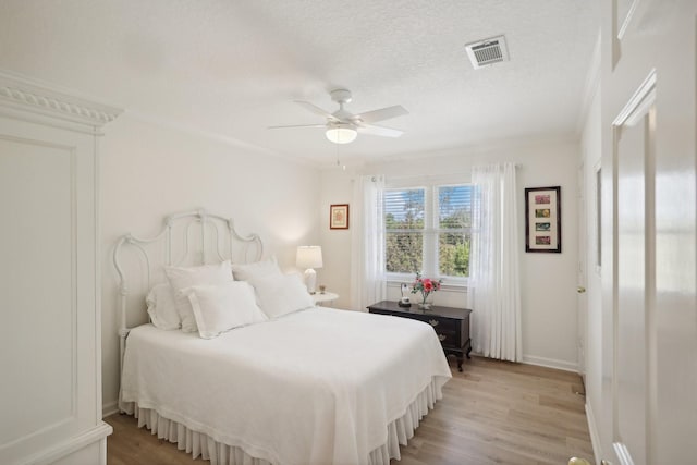 bedroom with a textured ceiling, ceiling fan, ornamental molding, and light hardwood / wood-style flooring