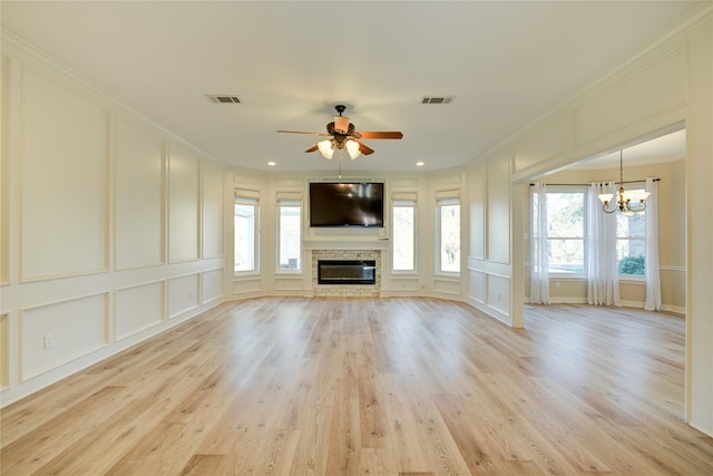 unfurnished living room with light hardwood / wood-style floors, a stone fireplace, crown molding, and ceiling fan with notable chandelier