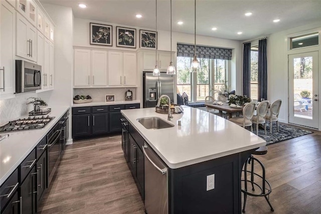 kitchen with sink, an island with sink, appliances with stainless steel finishes, and white cabinetry