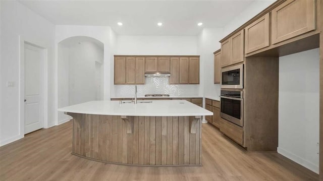 kitchen featuring sink, appliances with stainless steel finishes, a center island with sink, and light wood-type flooring