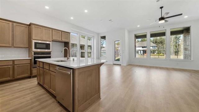 kitchen featuring sink, stainless steel appliances, a center island with sink, and light wood-type flooring