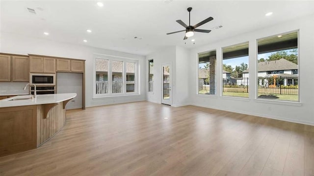 unfurnished living room with sink, ceiling fan, a healthy amount of sunlight, and light hardwood / wood-style flooring