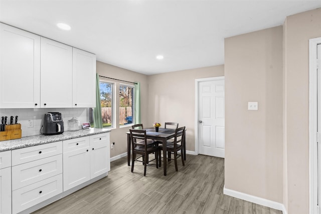 kitchen with tasteful backsplash, white cabinetry, light stone counters, and light hardwood / wood-style floors