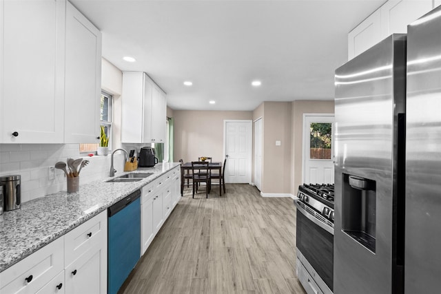 kitchen featuring sink, appliances with stainless steel finishes, white cabinetry, tasteful backsplash, and light stone countertops