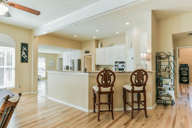 kitchen with appliances with stainless steel finishes, light wood-type flooring, light stone countertops, kitchen peninsula, and white cabinetry