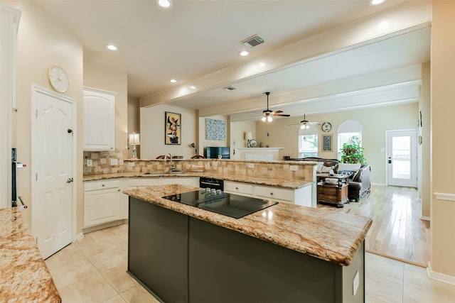 kitchen with kitchen peninsula, light stone countertops, a kitchen island, backsplash, and white cabinets