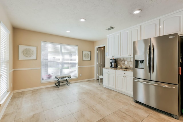 kitchen featuring light stone countertops, light tile patterned floors, stainless steel fridge, white cabinets, and backsplash