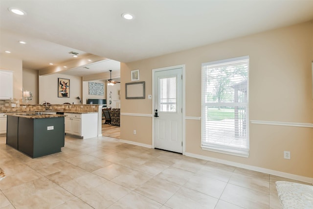 kitchen featuring beamed ceiling, kitchen peninsula, ceiling fan, a kitchen island, and white cabinets