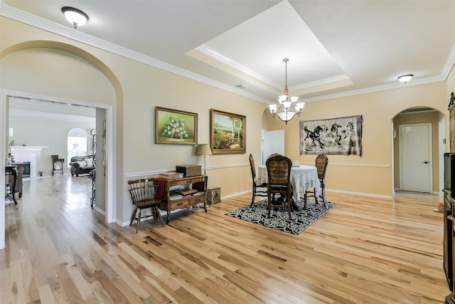 dining room featuring a raised ceiling, a chandelier, light wood-type flooring, crown molding, and a fireplace