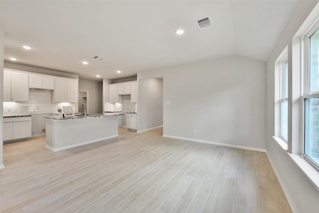 kitchen featuring vaulted ceiling, white cabinetry, light hardwood / wood-style floors, and a kitchen island with sink