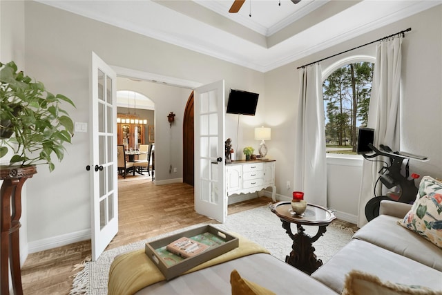 living room featuring ornamental molding, light wood-type flooring, a raised ceiling, and french doors