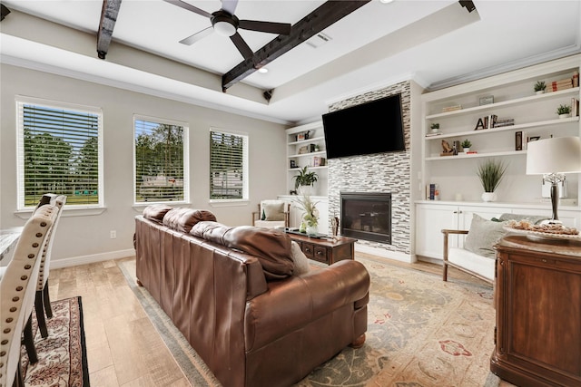 living room featuring a stone fireplace, beamed ceiling, light hardwood / wood-style floors, ornamental molding, and ceiling fan