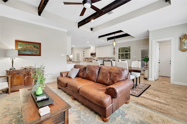 living room featuring light hardwood / wood-style floors, beam ceiling, ceiling fan, and ornamental molding