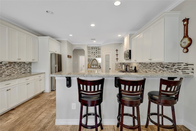 kitchen with white cabinets, stainless steel appliances, a kitchen bar, and light stone countertops