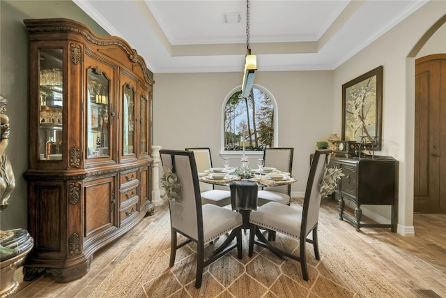 dining space with a raised ceiling, ornamental molding, and light hardwood / wood-style floors