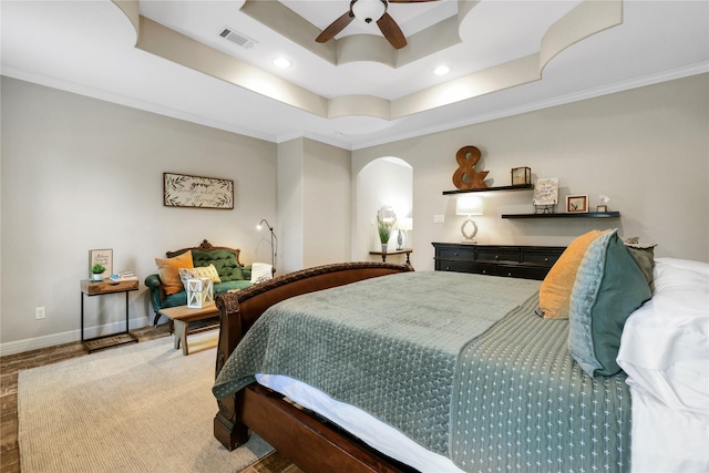 bedroom featuring ceiling fan, ornamental molding, hardwood / wood-style flooring, and a tray ceiling