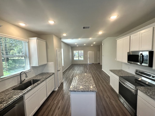 kitchen with white cabinets, stainless steel appliances, dark stone counters, dark hardwood / wood-style flooring, and sink