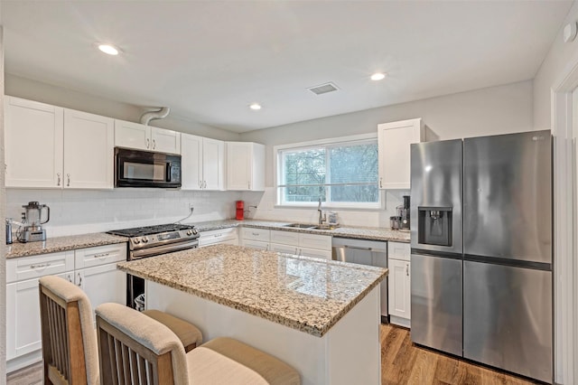 kitchen with stainless steel appliances, a center island, white cabinets, and sink