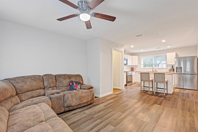 living room featuring ceiling fan, light hardwood / wood-style flooring, and sink