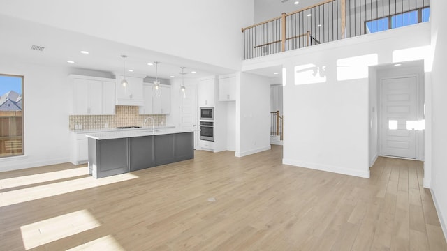 kitchen featuring decorative light fixtures, white cabinetry, an island with sink, decorative backsplash, and stainless steel oven