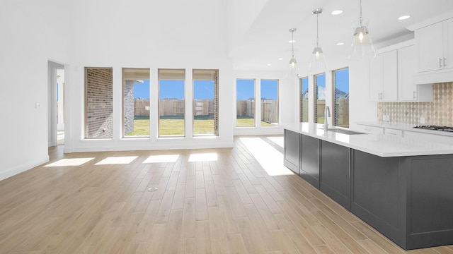 kitchen featuring a large island, decorative backsplash, white cabinets, decorative light fixtures, and sink