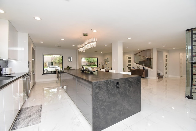 kitchen with sink, a large island, white cabinetry, stainless steel dishwasher, and hanging light fixtures