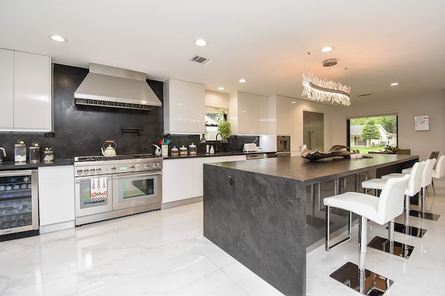 kitchen with white cabinets, wall chimney exhaust hood, double oven range, and hanging light fixtures