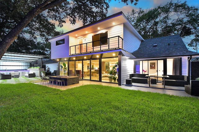 back house at dusk featuring a lawn, a balcony, a jacuzzi, a patio, and a fire pit