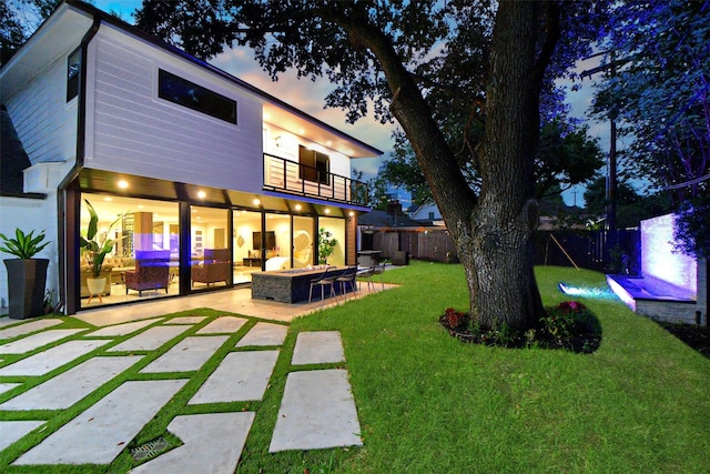 back house at dusk featuring a balcony, a lawn, a fire pit, and a patio area