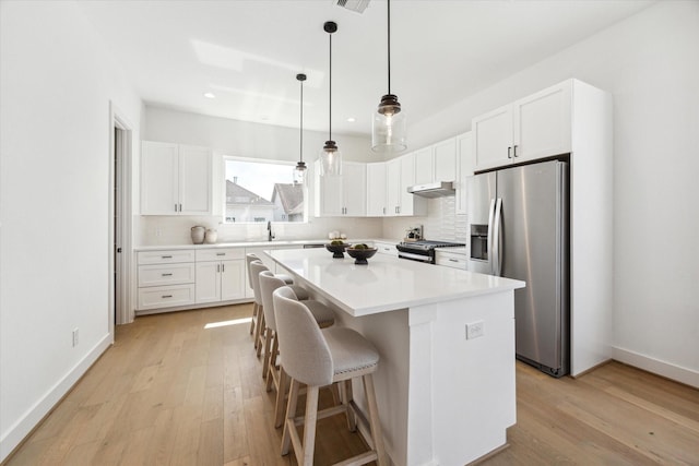 kitchen with a center island, appliances with stainless steel finishes, light wood-style floors, a sink, and under cabinet range hood