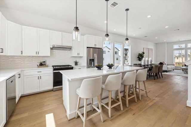 kitchen with dishwashing machine, under cabinet range hood, range with electric stovetop, visible vents, and stainless steel fridge