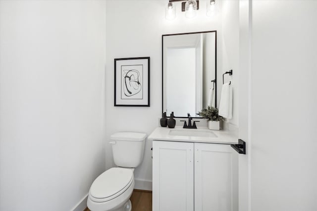 half bath with toilet, baseboards, and vanity