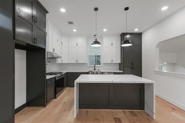 kitchen with stainless steel gas stove, decorative light fixtures, light wood-type flooring, light stone counters, and a kitchen island