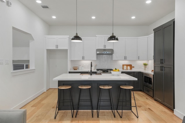 kitchen with appliances with stainless steel finishes, white cabinetry, hanging light fixtures, a kitchen island with sink, and sink