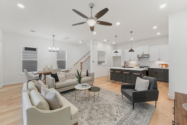 living room with sink, light wood-type flooring, and ceiling fan with notable chandelier